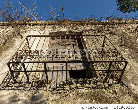 Low angle view of a wrought iron balcony with shuttered window on old wall in sunny location Low angle view of a wrought iron balcony with shuttered window on old wall in sunny location 141969256