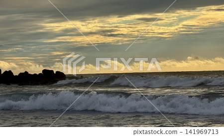 Ocean waves breaking near rocky breakwater at sunset under dramatic cloudy sky Ocean waves breaking near rocky breakwater at sunset under dramatic cloudy sky 141969713