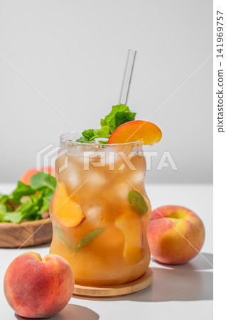 Refreshing peach iced cocktail or tea with mint in a glass on a light background with shadow. Refreshing peach iced cocktail or tea with mint in a glass on a light background with shadow. 141969757