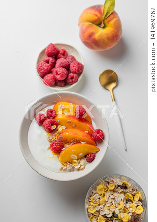 Natural greek yogurt with muesli, raspberry, peach and honey in a bowl on a white background Natural greek yogurt with muesli, raspberry, peach and honey in a bowl on a white background 141969762