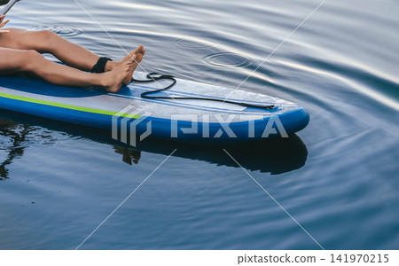 Barefoot Woman Resting on Stand Up Paddleboard Barefoot Woman Resting on Stand Up Paddleboard 141970215