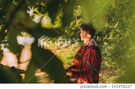 Man Musician Playing Acoustic Guitar in Forest Man Musician Playing Acoustic Guitar in Forest 141970227