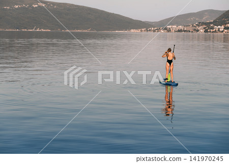 Woman Standing On Paddleboard in Bay of Kotor Woman Standing On Paddleboard in Bay of Kotor 141970245