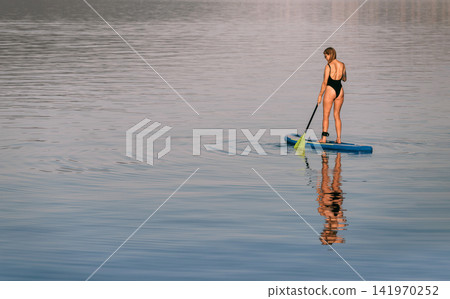 Woman Standing on Paddleboard Gliding over Sea Woman Standing on Paddleboard Gliding over Sea 141970252