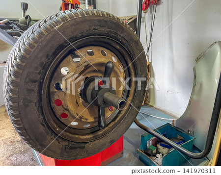 Used car wheel mounted on balancing machine in auto repair shop, ready for diagnostics, rotation or seasonal tire change Used car wheel mounted on balancing machine in auto repair shop, ready for diagnostics, rotation or seasonal tire change 141970311