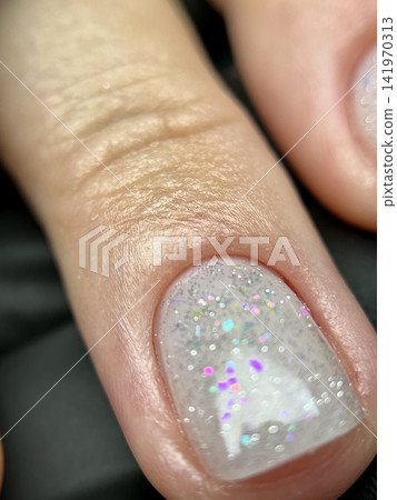 Close-up of glitter gel nail polish on natural short nail in beauty salon. Extreme macro photo of a clean natural short nail 141970313