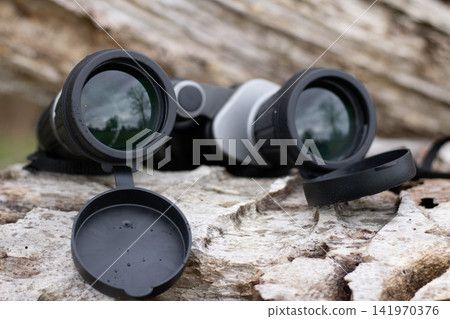 Black binoculars on a fallen tree, travel concept Black binoculars on a fallen tree, travel concept 141970376