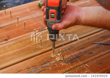 Man nailing the wooden boards to fix the terrase Man nailing the wooden boards to fix the terrase 141970429