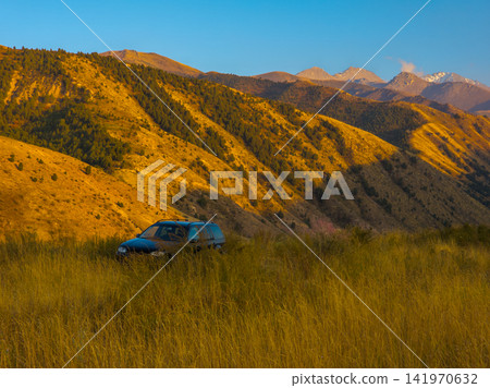 SUV in tall grass with golden hills and mountains in background SUV in tall grass with golden hills and mountains in background 141970632