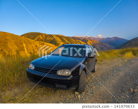 Black Station Wagon on Gravel Road in Mountain Landscape Black Station Wagon on Gravel Road in Mountain Landscape 141970633