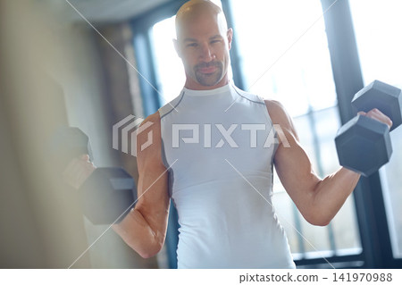 Man, weight lifting and exercise or portrait for fitness with dumbbell, workout challenge and strong muscle. Bodybuilder, pro athlete or strength training with confidence for power competition in gym Man, weight lifting and exercise or portrait for fitness with dumbbell, workout challenge and strong muscle. Bodybuilder, pro athlete or strength training with confidence for power competition in gym 141970988