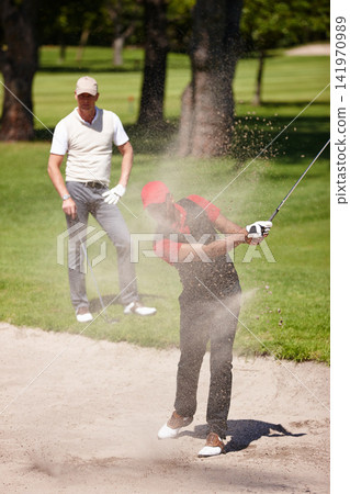 Man, golf and club for sports and swing for fitness, practice and hobby in summer outdoor. Golfer or player with friend and training in sand bunker for game challenge, recreation or workout on lawn Man, golf and club for sports and swing for fitness, practice and hobby in summer outdoor. Golfer or player with friend and training in sand bunker for game challenge, recreation or workout on lawn 141970989