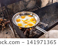 View to cooking eggs in a stainless steel pan over an open fire outdoors 141971365