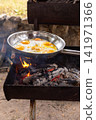 Cooking eggs in a stainless steel pan over an open fire outdoors 141971366