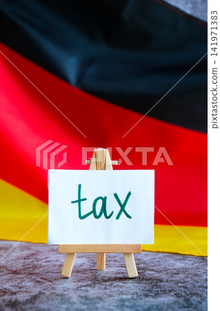 Paper note with words TAX on National symbol of Germany. German wave silky flag background. Tax planning system and economy policy Paper note with words TAX on National symbol of Germany. German wave silky flag background. Tax planning system and economy policy 141971383