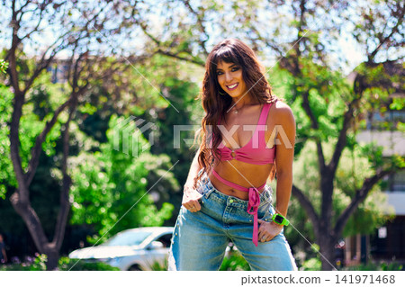 Beautiful, mature, Latina, Arab woman with dark hair, posing happily and inviting others to dance in an outdoor park. She's wearing a colorful retro pink outfit and jeans, and has makeup on. Beautiful, mature, Latina, Arab woman with dark hair, posing happily and inviting others to dance in an outdoor park. She's wearing a colorful retro pink outfit and jeans, and has makeup on. 141971468