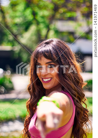 Beautiful, mature Latina woman with dark hair, posing and poised to dance in an outdoor park. She wears retro pink clothing and jeans, and makeup. Style, attitude, beauty, and freedom. Beautiful, mature Latina woman with dark hair, posing and poised to dance in an outdoor park. She wears retro pink clothing and jeans, and makeup. Style, attitude, beauty, and freedom. 141971469