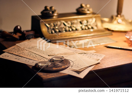 Details of old documents handwritten with quill and ink, resting on a desk, next to the author's antique glasses, illuminating the documents. History, antiquity, relics Details of old documents handwritten with quill and ink, resting on a desk, next to the author's antique glasses, illuminating the documents. History, antiquity, relics 141971512