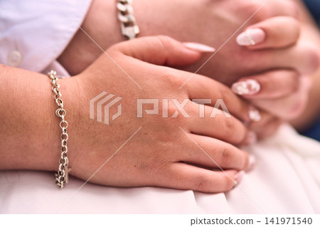 A view of a couple's hands, very affectionate, with details on the bride's nails, featuring figures and designs, their hands intertwined. Romance, engaged couple, union, love. 141971540