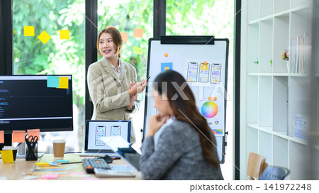 Young Gen Z Asian Female Developer Presenting Mobile App UI UX Design to Colleague on Whiteboard in Modern Office Young Gen Z Asian Female Developer Presenting Mobile App UI UX Design to Colleague on Whiteboard in Modern Office 141972248