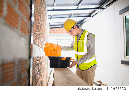Young Asian Engineer Opening Toolbox at Construction Site Wearing Yellow Hard Hat and Safety Vest Young Asian Engineer Opening Toolbox at Construction Site Wearing Yellow Hard Hat and Safety Vest 141972250