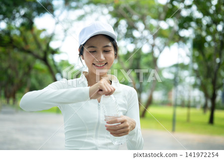 Young Asian Woman Opening Water Bottle After Outdoor Exercise in Park 141972254
