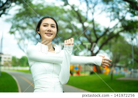 Young Asian Woman Stretching Arms in Green Park Before Workout, Smiling and Happy Young Asian Woman Stretching Arms in Green Park Before Workout, Smiling and Happy 141972256