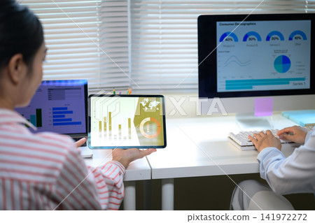 Business professionals analyzing data analytics dashboard on tablet and computer monitors in modern office Business professionals analyzing data analytics dashboard on tablet and computer monitors in modern office 141972272