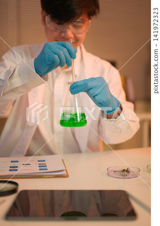 Scientist carefully mixes green solution in a flask Scientist carefully mixes green solution in a flask 141972323
