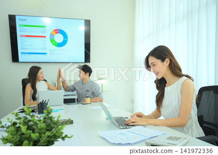 Smiling businesswoman reviewing report in laptop during team meeting Smiling businesswoman reviewing report in laptop during team meeting 141972336