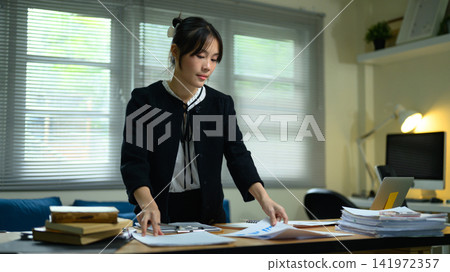 Young Asian Businesswoman Sorting Documents for Analysis at Office Desk Young Asian Businesswoman Sorting Documents for Analysis at Office Desk 141972357