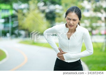 Asian Woman Runner Experiencing Side Stitch or Stomach Pain While Jogging in Park Asian Woman Runner Experiencing Side Stitch or Stomach Pain While Jogging in Park 141972454
