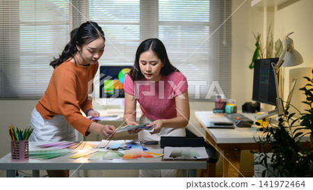 Two Asian Female Creative Designers Reviewing Color Swatches Together in a Modern Design Studio Office Two Asian Female Creative Designers Reviewing Color Swatches Together in a Modern Design Studio Office 141972464