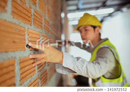 Engineer in Yellow Hard Hat Inspecting Brick Wall at Construction Site 141972552