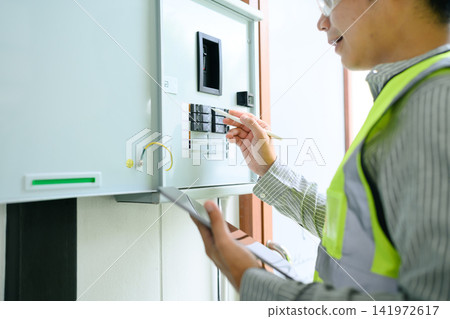 Closeup Electrician Inspecting Electrical Control Panel with Tablet and Pen During House Maintenance Closeup Electrician Inspecting Electrical Control Panel with Tablet and Pen During House Maintenance 141972617