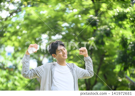Fresh and Cheerful Young Asian Man Exercising Outdoors in Park Holding Water Bottle with Energetic Pose Fresh and Cheerful Young Asian Man Exercising Outdoors in Park Holding Water Bottle with Energetic Pose 141972681