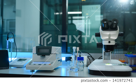 Modern Scientific Laboratory Workbench with Stereo Microscope, Analytical Balance, and Glassware in Blue-Tinted Research Facility Modern Scientific Laboratory Workbench with Stereo Microscope, Analytical Balance, and Glassware in Blue-Tinted Research Facility 141972741
