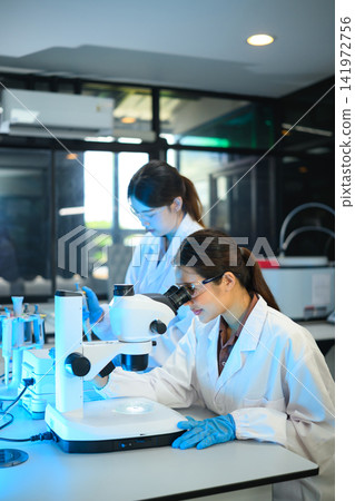 Two Asian Female Scientists Working in Modern Laboratory with Microscope and Research Equipment Two Asian Female Scientists Working in Modern Laboratory with Microscope and Research Equipment 141972756