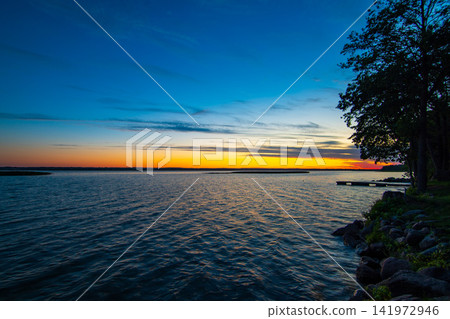 Colorful Sunset over Calm Lake with Wooden Pier and Two People Standing on the Dock Colorful Sunset over Calm Lake with Wooden Pier and Two People Standing on the Dock 141972946