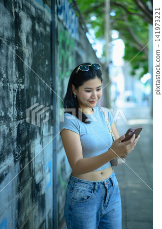 Young woman using smartphone while walking in green urban area Young woman using smartphone while walking in green urban area 141973221