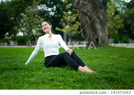 Young Asian Woman in Activewear Relaxing on Green Grass in Park with Happy Smile Young Asian Woman in Activewear Relaxing on Green Grass in Park with Happy Smile 141973263