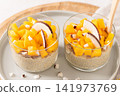 Two glasses of creamy chia seed pudding topped with vibrant diced mango and fresh coconut slices served on a gray plate for a healthy breakfast or nutritious tropical snack in a bright aesthetic 141973769