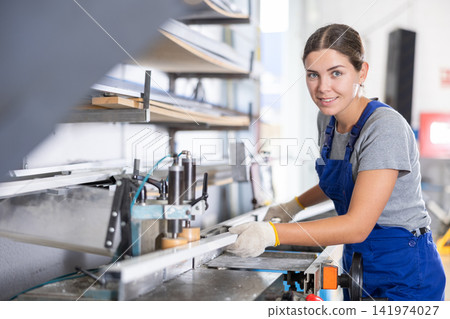 Smiling female machinist operating industrial profile cutting machine Smiling female machinist operating industrial profile cutting machine 141974027