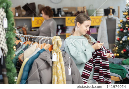 Teenage girl chooses sweater in clothing store Teenage girl chooses sweater in clothing store 141974054