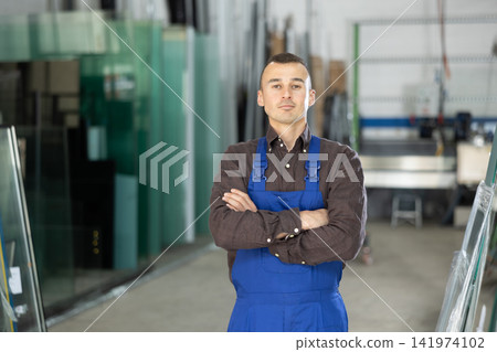 Portrait of positive man in blue overalls in window glass production workshop Portrait of positive man in blue overalls in window glass production workshop 141974102
