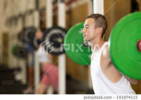 Man in activewear exercising with barbell during group workout in gym center Man in activewear exercising with barbell during group workout in gym center 141974115