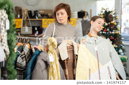 Adult woman and teenage girl choosing coat or down jacket Adult woman and teenage girl choosing coat or down jacket 141974157