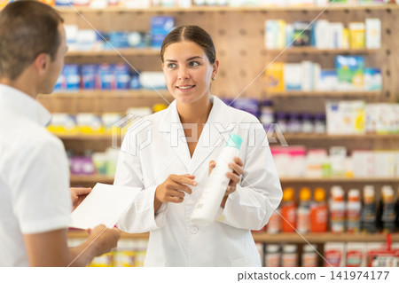 Female consultant pharmacist holds bottle of shampoo and offers to man client to purchase remedy 141974177