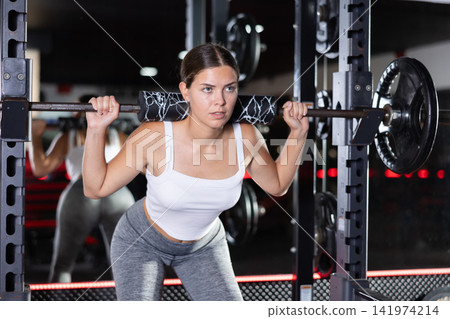 Sporty girl performing set of exercises with barbell during intense workout. Concept of weight training Sporty girl performing set of exercises with barbell during intense workout. Concept of weight training 141974214