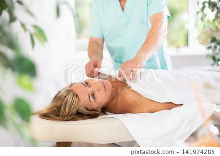 the man ensures the woman is comfortably covered with a towel for the massage. the man ensures the woman is comfortably covered with a towel for the massage. 141974285